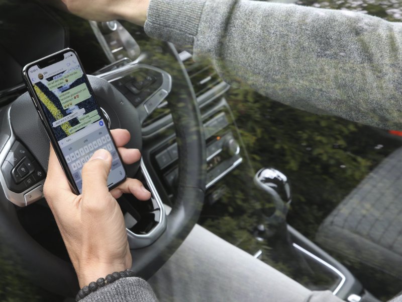 Nachricht tippen am Autolenkrad Hand tippt eine Nachricht auf dem Smartphone direkt hinter dem Lenkrad im Auto.